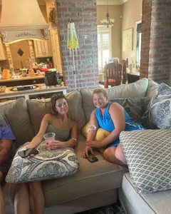 Two women smiling on a sofa at a house gathering, each with an IV drip in her arm